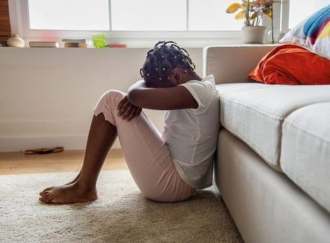 A young girl curled on the floor against a couch